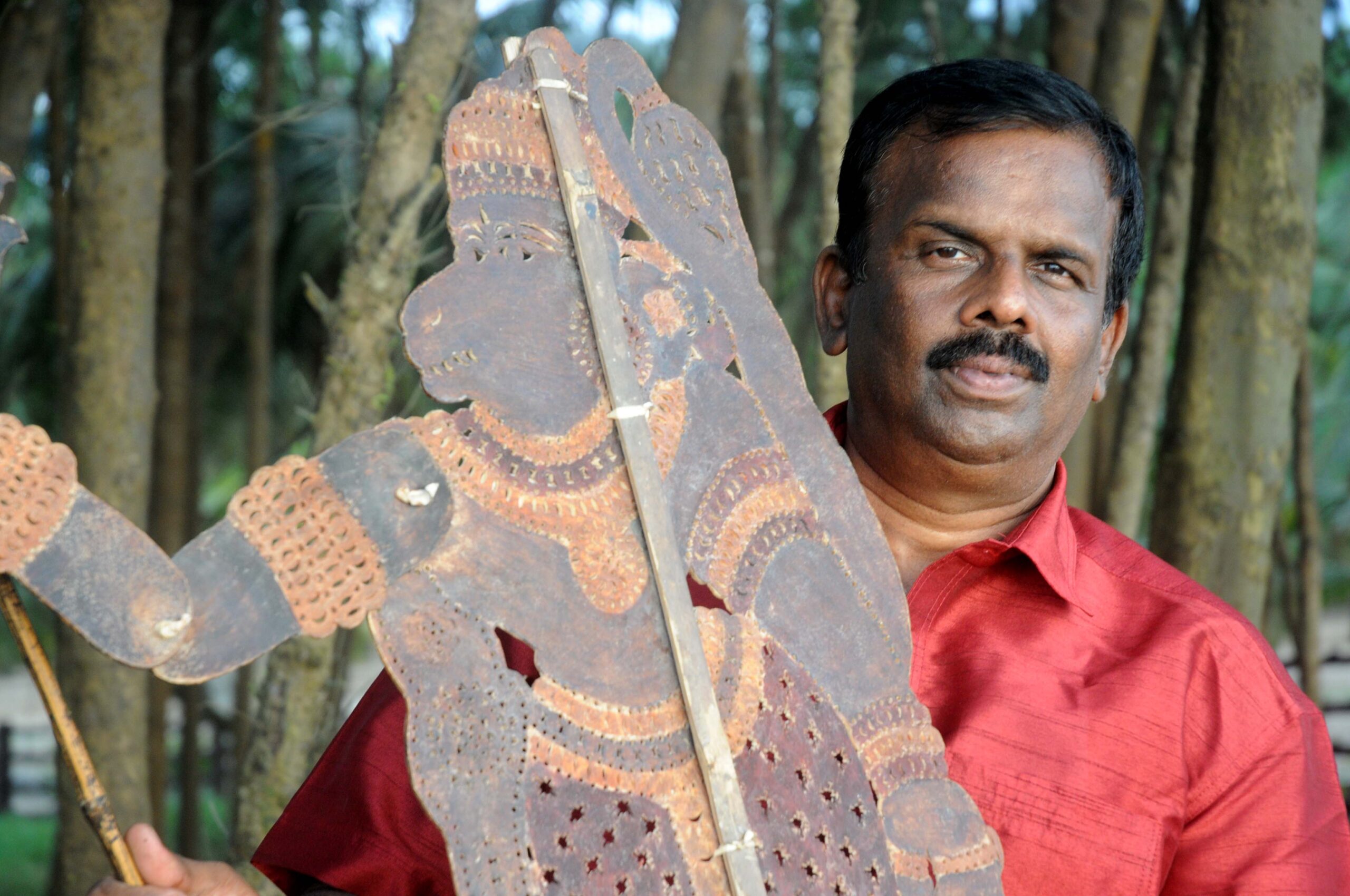 An artist from the Pulavar puppetry tradition holding a decorated leather figure